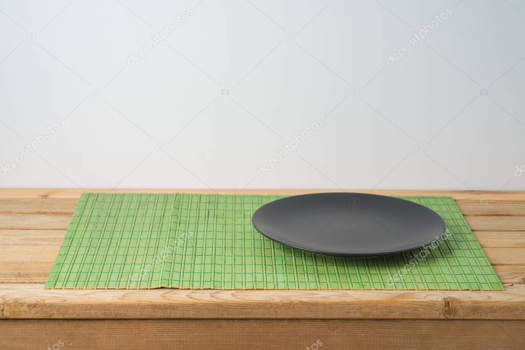 Black empty plate and bamboo placemat on wooden table. Chinese k