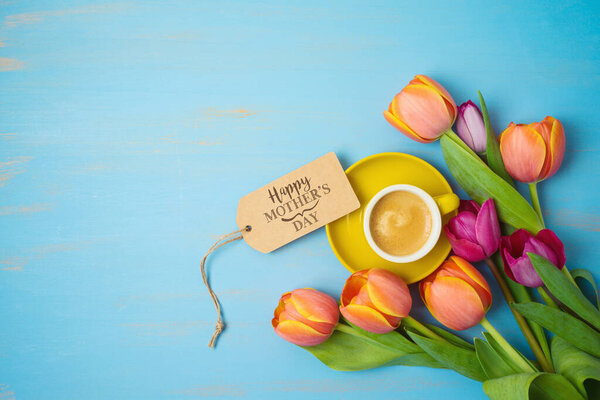 Happy Mother's day concept with coffee cup and beautiful tulip flowers on wooden background. Top view from above