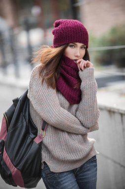 Sıcak bir kazak, kırmızı bere ve atkı ve bir sırt çantası onun omuz üzerinde güzel bir genç kız portresi