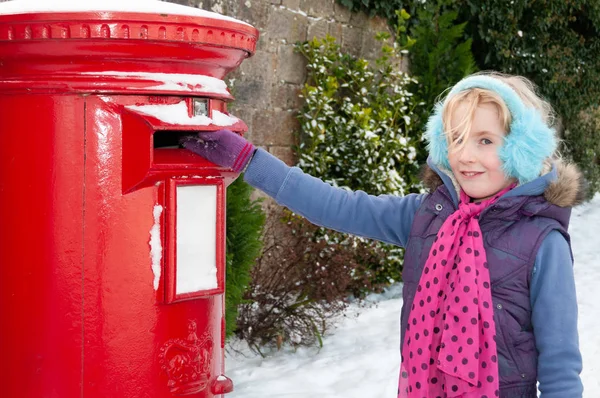 Gelukkig jong blond meisje in blauw oor moffen in een besneeuwde omgeving posten van haar brief naar Santa — Stockfoto