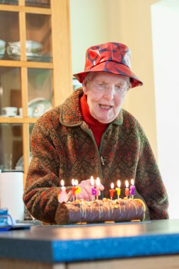 Kırmızı şapkalı yaşlı kadın doğum günü pastasındaki mumları sayıyor.