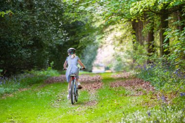 Girl in school uniform and cycle helmet riding bike along a tree lined country track clipart