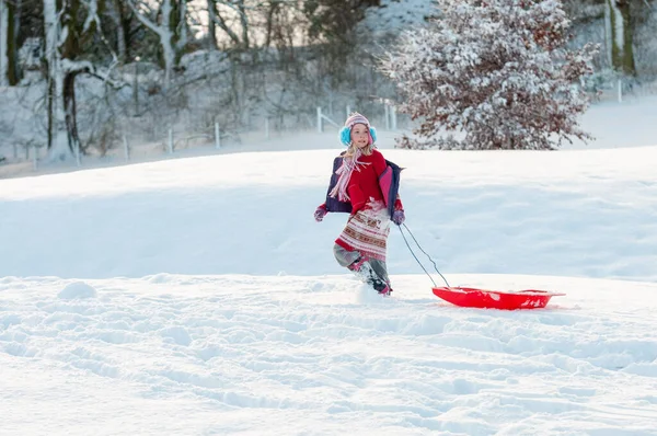 Жорстоко одягнена молода дівчина тягне за собою санки через глибокий сніг в сільській місцевості — стокове фото