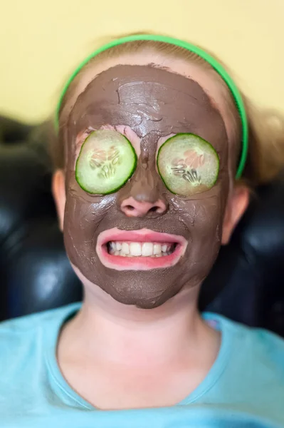 Happy young girl with a face pack on and cucumber slices on her eyes