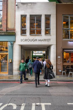 Müşteriler ve bir sokak temizleyicisi Londra 'daki Borough Market' e giriş kapısından geçiyor.