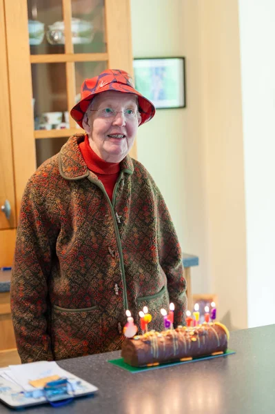 Elderly woman in a red floppy hat with a birthday cake covered in lit candles