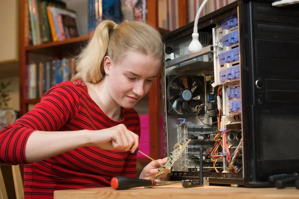 Happy teenage girl using a screwdriver on an expansion card printed circuit board from an open PC