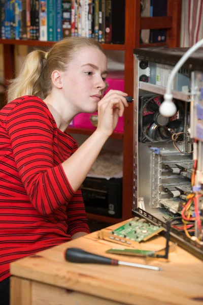 Teenage girl using a screwdriver to dismantle an open PC