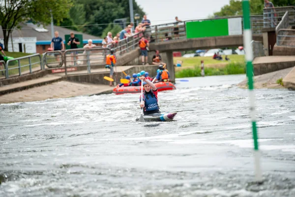 GB Canoe Slalom Athlete paddling towards camera with a raft and spectators in the background. Women's C1W class
