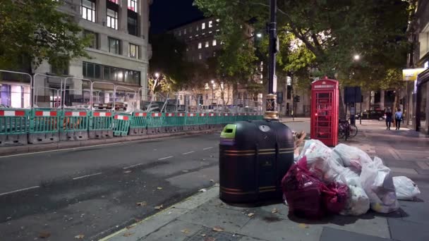 ロンドン 2019年9月26日 車や道路工事を背景に 夜にゴミ箱と伝統的な赤い電話ボックスの横に積み上げられたゴミ袋の広いショット — ストック動画