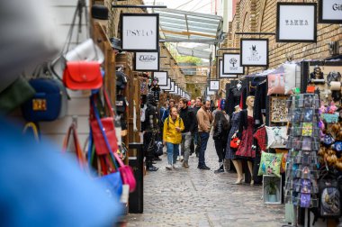 30 EPTEMBER 2019: Camden Lock Marketleri 'nde market tezgahlarıyla dolu kapalı bir caddede alışveriş yapanlar
