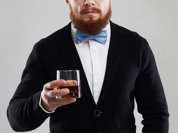 Hombre barbudo disfrutando de un brandy o whiskey.Elegant hombre de traje y corbata bebiendo un whisky en el estudio — Foto de Stock