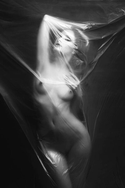 Dancing girl behind a polyethylene film. beautiful nude woman. Fine-art photo. figure of a naked woman behind a transparent curtain