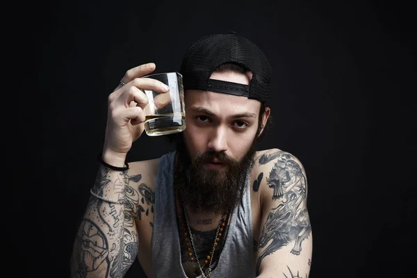 tattooed man in hat drinking a whiskey