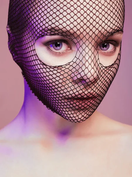 Beautiful Woman in Net on her Face lighted in pink. Pretty Girl in lace mask