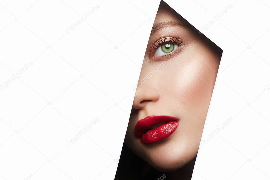 young beautiful woman with makeup. make-up artist concept. A girl with beautiful bright green eyes, looks into hole of white paper