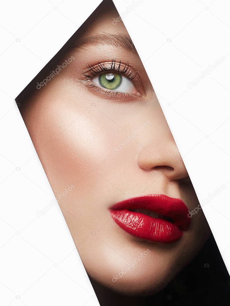 young beautiful woman with makeup. make-up artist concept. A girl with beautiful bright green eyes, looks into hole of white paper