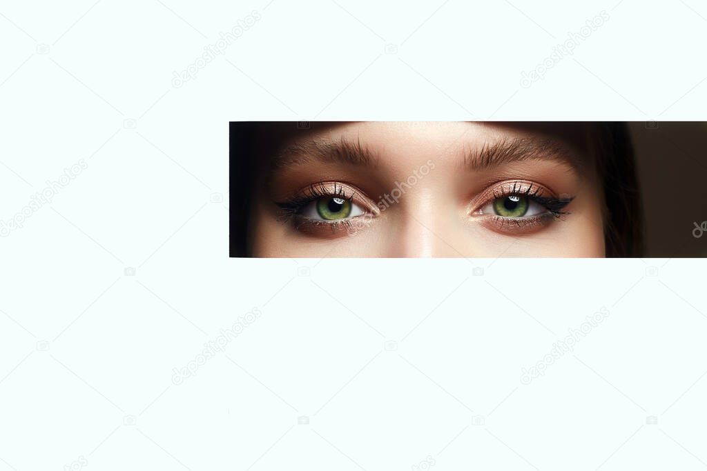 beautiful eyes peeping into the crack. young beautiful woman. make-up artist concept. A girl with beautiful bright green eyes with shining shadows, looks into the hole of white paper