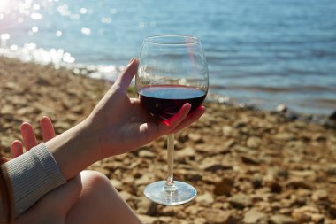 Sahilde elinde bir bardak kırmızı şarap tutan bir kız. Şaraplı kadın eli. Tatil