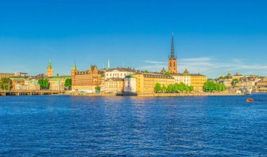 Riddarholmen adasının panoramik manzarası, Riddarholm Kilisesi kuleleri, tipik İsveçli gotik binalar, Birger kavanozları parçalanmış, Malaren Gölü suyu, mavi açık gökyüzü, Stockholm, İsveç