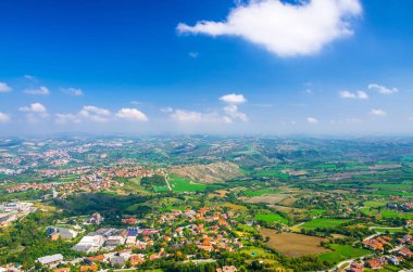 Vadi, yeşil tepeler, tarlalar ve mavi gökyüzü beyaz bulutlarıyla kaplı San Marino banliyö bölgesinin köylerinin panoramik manzarası. San Marino kalesinden görüntü