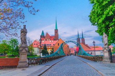 Cobblestone yolu ve Odra Oder nehri üzerindeki Tumski köprüsü, Kutsal Haç Koleji Kilisesi ve Wroclaw 'ın eski tarihi şehir merkezinde Vaftizci Aziz John Katedrali, akşam manzarası, Polonya