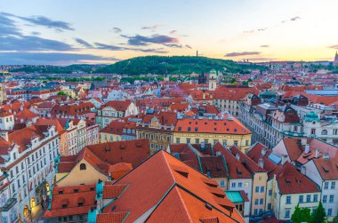 Prag Eski Kasabası 'nın (Stare Mesto) en iyi panoramik manzarası kırmızı kiremitli çatı binaları ve Petrin Tepesi bahçesi ile akşam günbatımında, Bohemya, Çek Cumhuriyeti