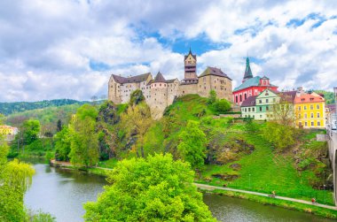 Madalyon Şatosu Hrad Loketi Gotik stil binası eğer Nehri üzerindeki dev kayalar ve Loket kasabasındaki renkli binalar, yeşil ağaçlar ve tepeler arka plan, Karlovy Vary Bölgesi, Batı Bohemya, Çek Cumhuriyeti