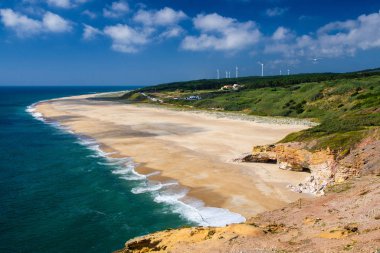 Portugal, Nazare in summer, coastline landscape of the Atlantic ocean in summer,  wide beaches with azure blue water of the Atlantica, cliffs of Nazare, dense greenery and windmills in the background