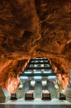 İsveç, Stockholm, 30 Mayıs 2018: Yeraltı metro tüneli istasyonu Radhuset (mavi hat, merkez istasyon) yürüyen merdiven ve turuncu kahverengi desenli mağaralar duvarlar ve tavan - modern sanat galerisi
