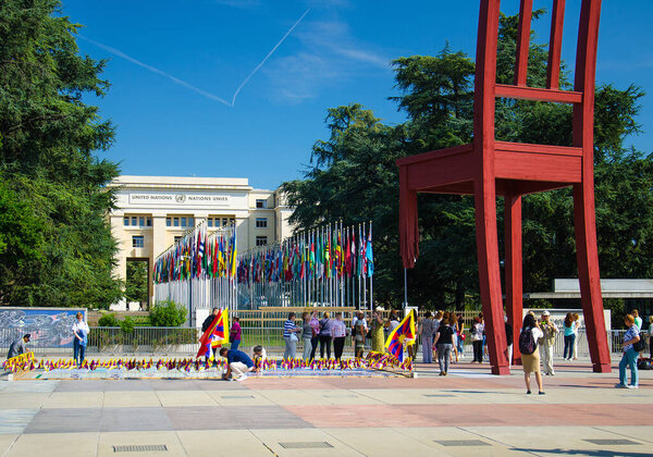 Geneva, Switzerland - September 14, 2016: Broken chair on the square of Nations and walking people in front of Palace of United nations building - Peace symbol in Geneva, Switzerland