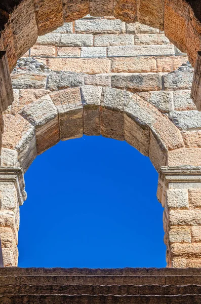 Blue clear sky through limestone brick arch window of The Verona Arena