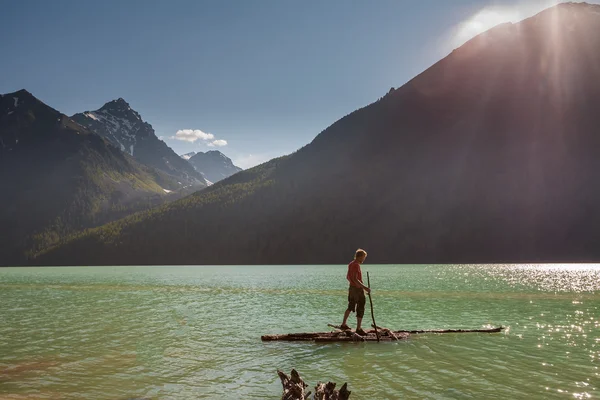 Man on wooden raft tries to cross the lake in high mountains — ストック写真