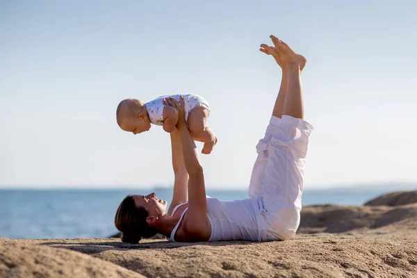 Una madre y un hijo están haciendo ejercicios de yoga en la orilla del mar de M — Foto de Stock