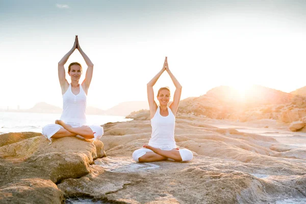 Dos hermanas están haciendo ejercicios de yoga en la orilla del mar de Mediterr — Foto de Stock