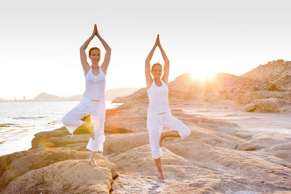 Dos hermanas están haciendo ejercicios de yoga en la orilla del mar de Mediterr — Foto de Stock