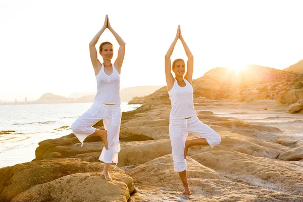 Dos hermanas están haciendo ejercicios de yoga en la orilla del mar de Mediterr — Foto de Stock