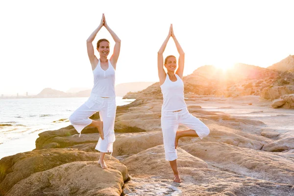 Dos hermanas están haciendo ejercicios de yoga en la orilla del mar de Mediterr — Foto de Stock
