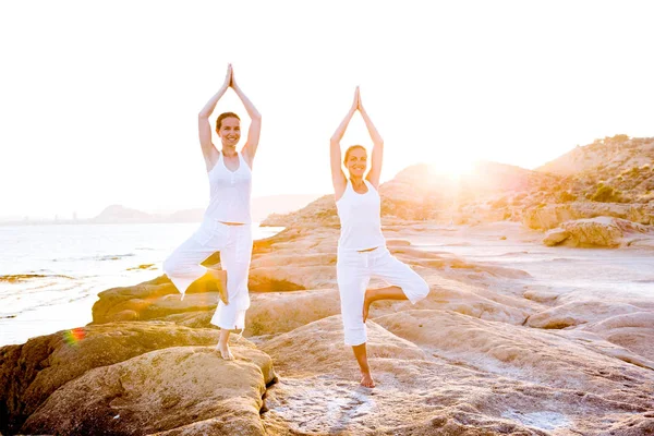 Dos hermanas están haciendo ejercicios de yoga en la orilla del mar de Mediterr — Foto de Stock