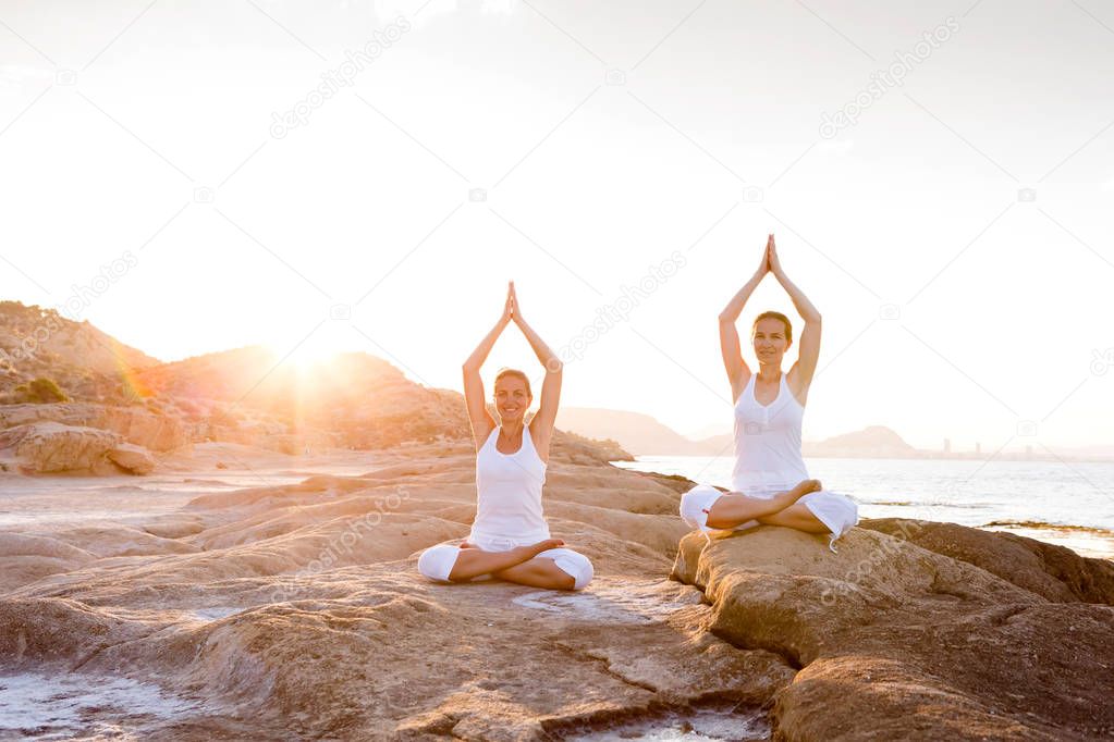 Two sisters are doing yoga exercises at the seashore of Mediterr