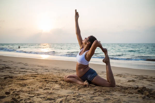Естественно выглядящая беременная женщина практикующая йогу на берегу моря — стоковое фото