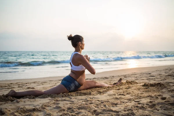 Mujer embarazada de aspecto natural practicando yoga en la orilla del mar a — Foto de Stock