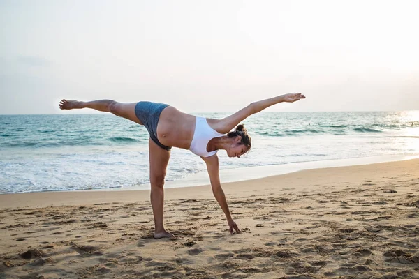 Mujer embarazada de aspecto natural practicando yoga en la orilla del mar a —  Fotos de Stock