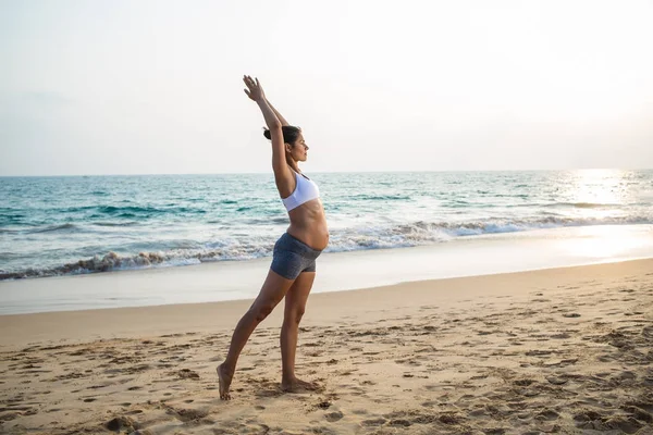 Mujer embarazada de aspecto natural practicando yoga en la orilla del mar a — Foto de Stock