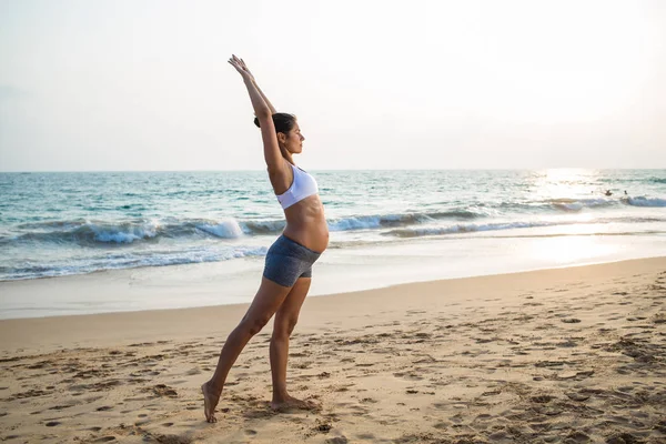 Mujer embarazada de aspecto natural practicando yoga en la orilla del mar a — Foto de Stock