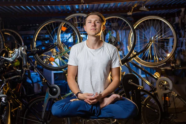 Young man is practicing yoga in garage with many bicycles behind