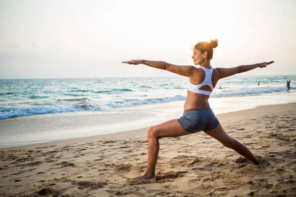 Mujer embarazada de aspecto natural practicando yoga en la orilla del mar a — Foto de Stock