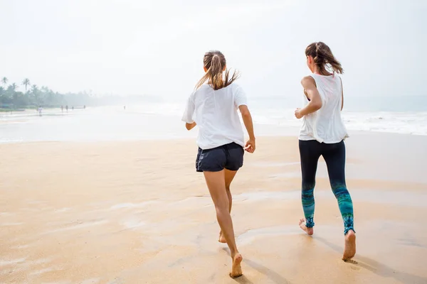 Две женщины бегают по берегу моря в пасмурный день — стоковое фото