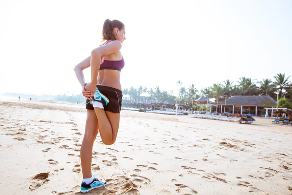 Kvinna löpare stretching ben muskler på stranden på sunrise — Stockfoto