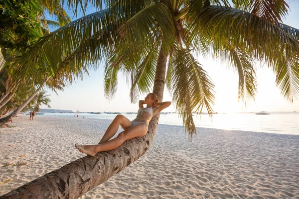 Perempuan terletak di pohon palem dekat laut saat matahari terbenam — Stok Foto